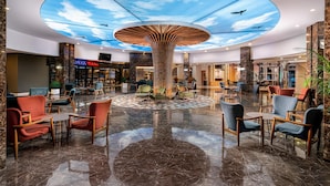A spacious lobby with a central wooden column, seating areas, and a ceiling with a sky and cloud design. - Avena Resort & Spa Hotel - All Inclusive  (Alanya)