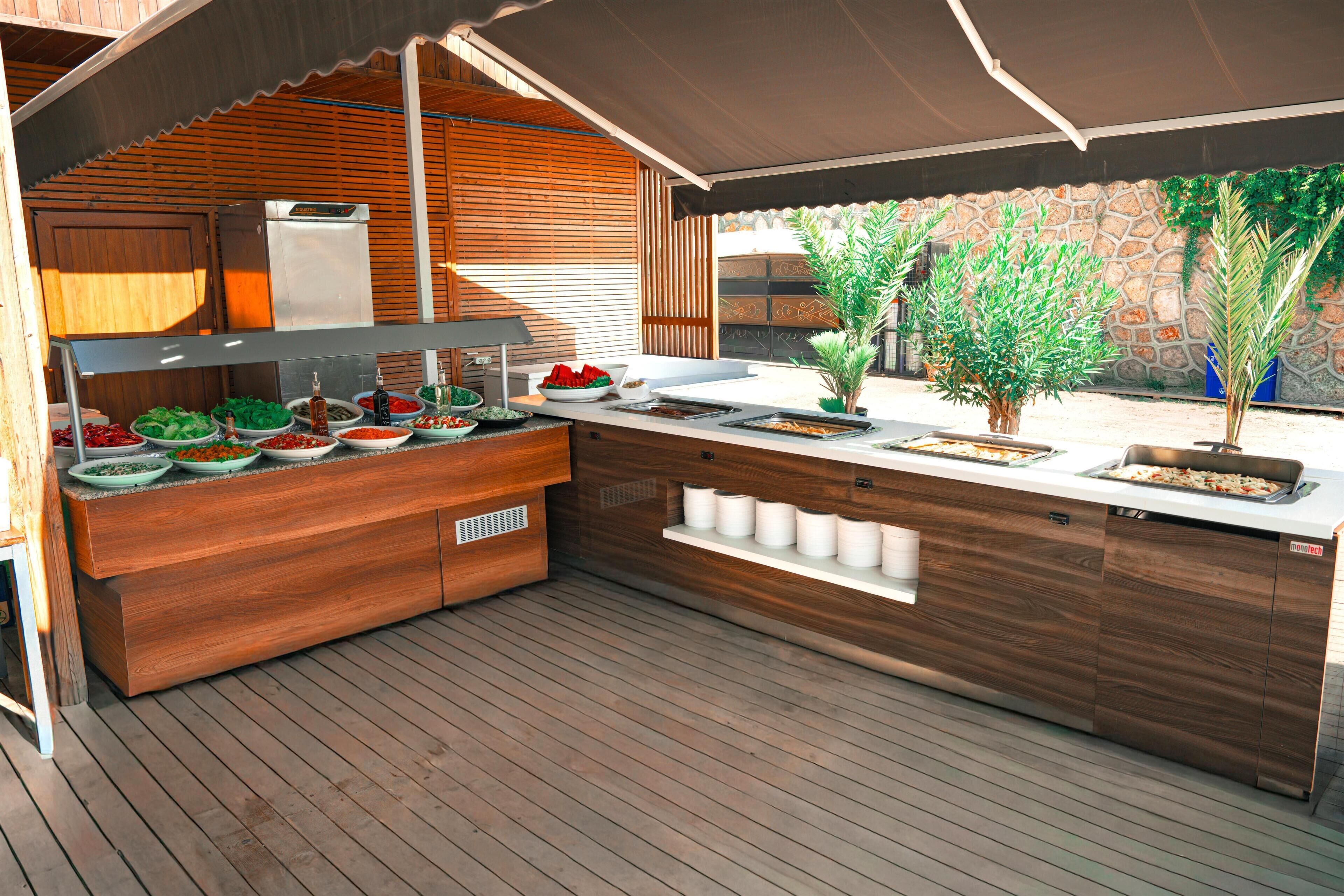 An outdoor kitchen with wooden cabinetry, a built-in grill, and various food items.