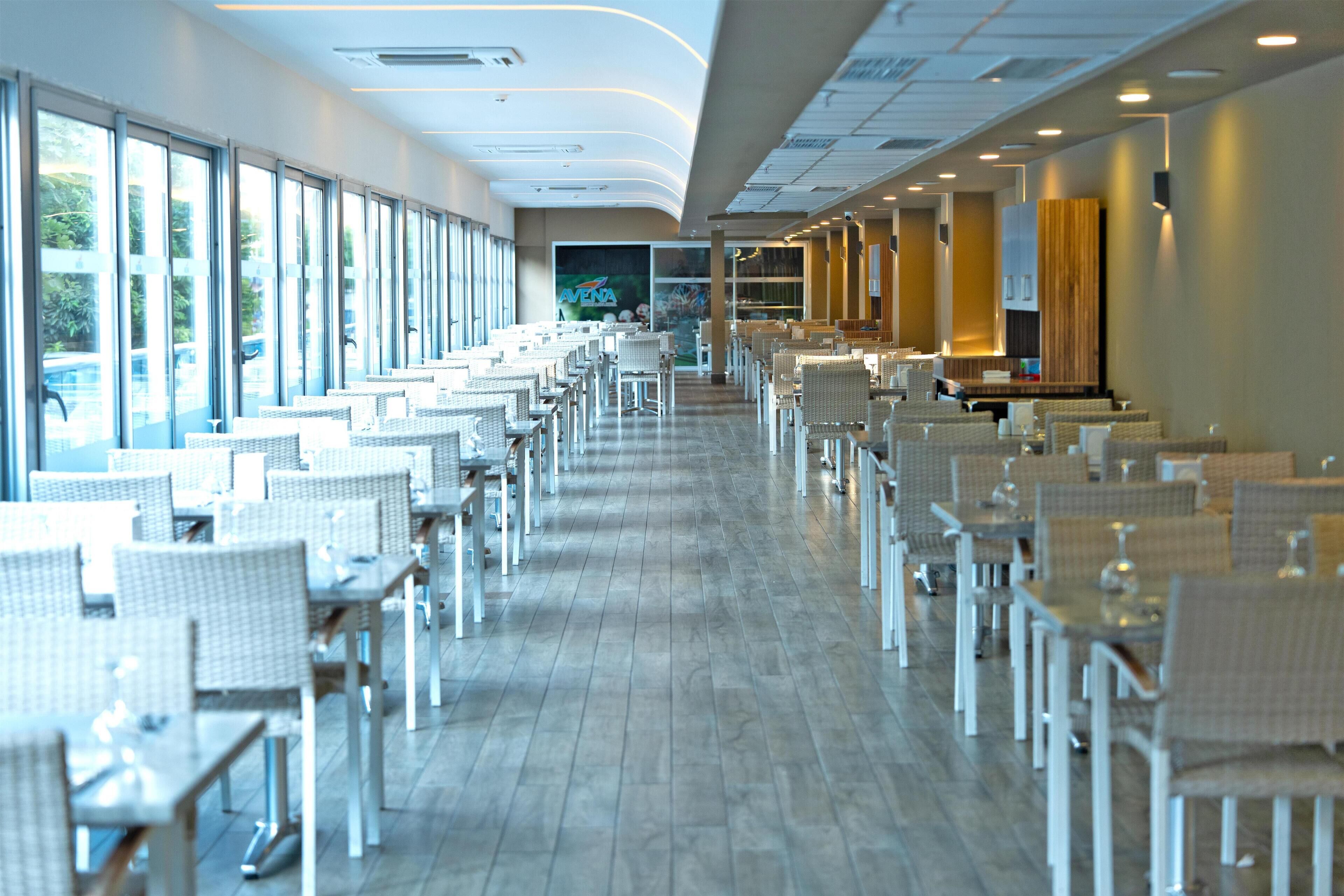 A spacious restaurant with long tables and chairs, large windows, and a modern interior design.