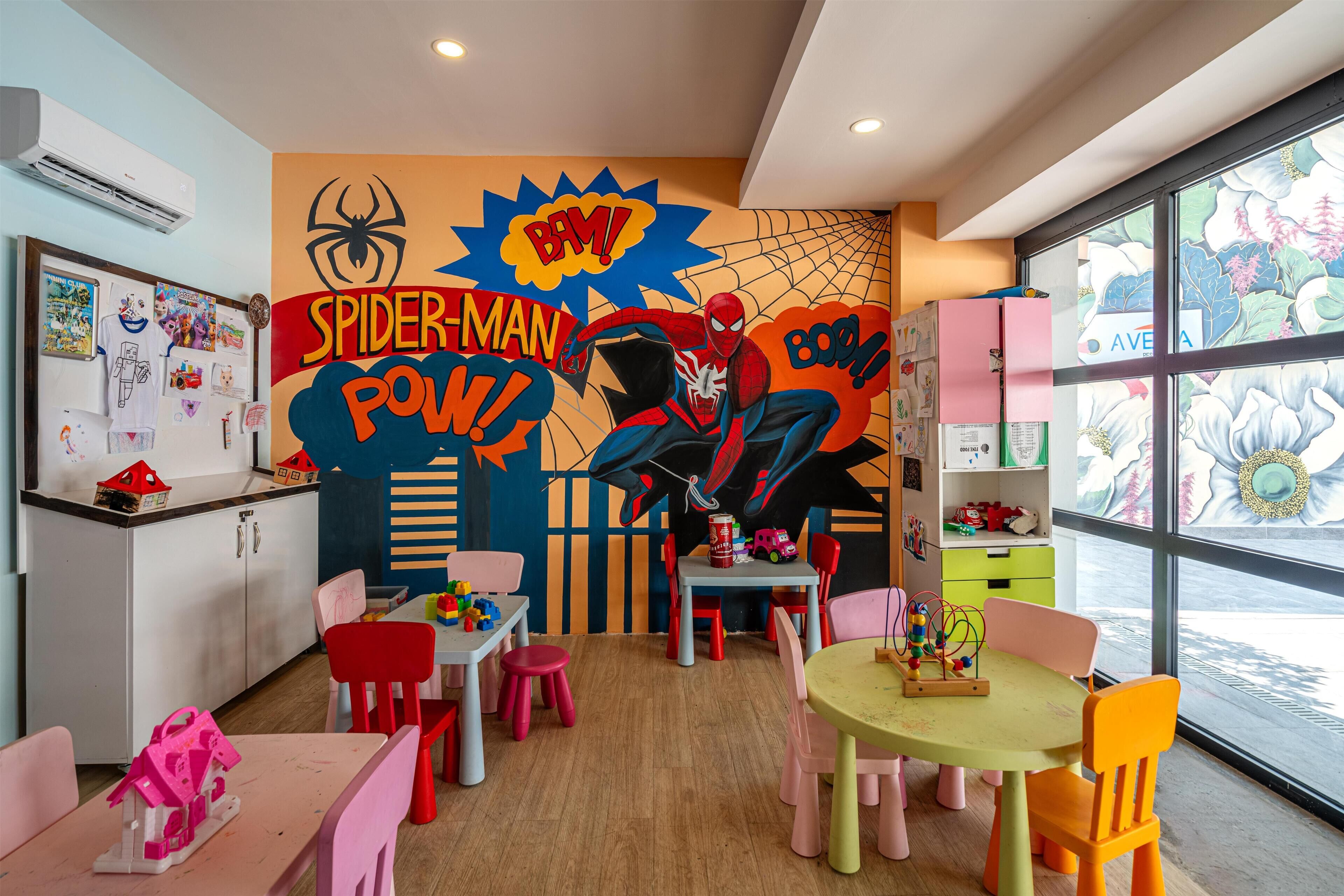 A children's playroom with a Spider-Man mural, colorful furniture, and a large window.