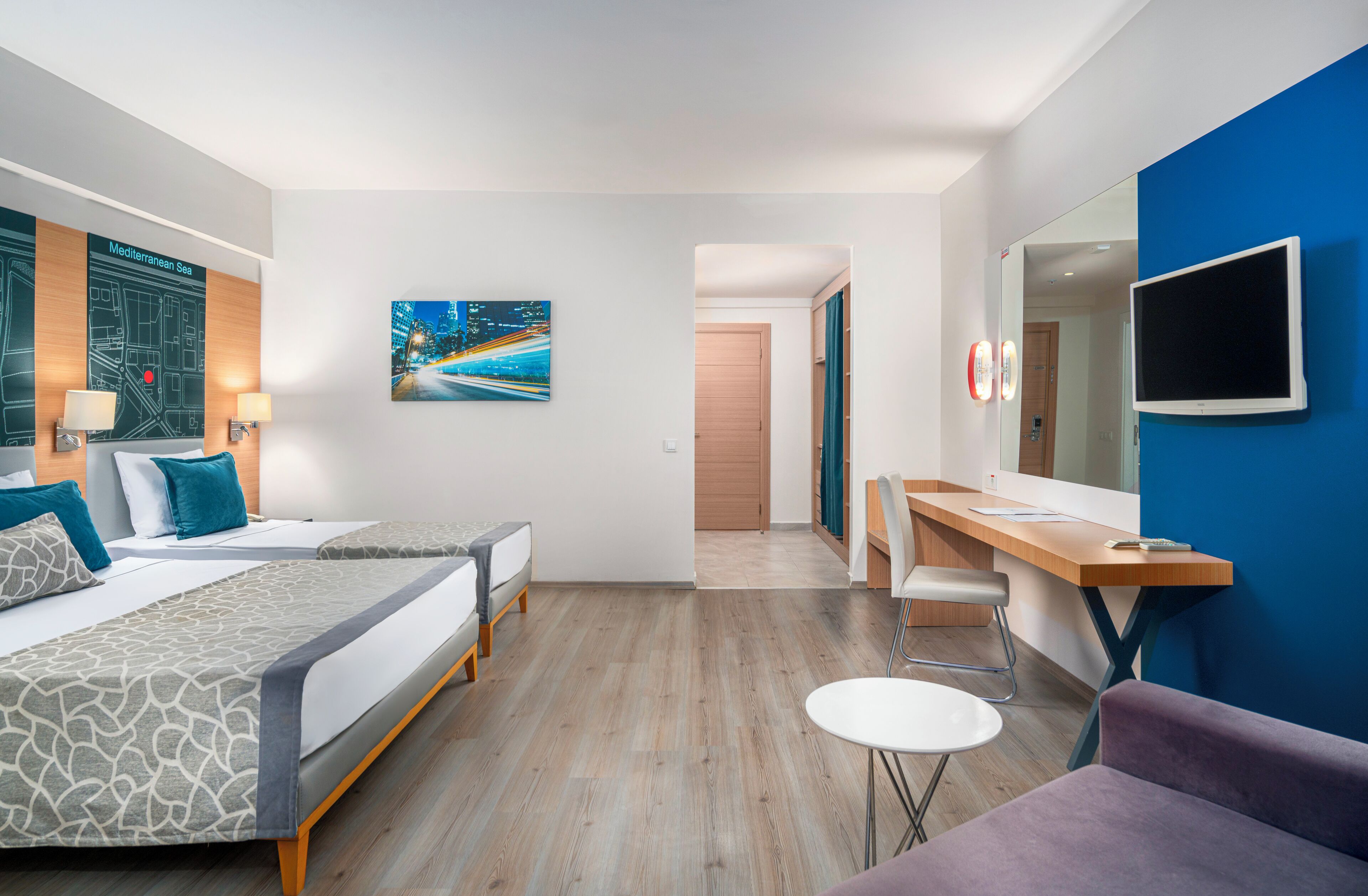 Une chambre d’hôtel avec deux lits, un bureau, une chaise, une télévision et un tableau au mur.