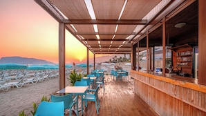 A beachside bar with wooden flooring and blue chairs, overlooking a beach with sun loungers and umbrellas. - Avena Resort & Spa Hotel - All Inclusive  (Alanya)