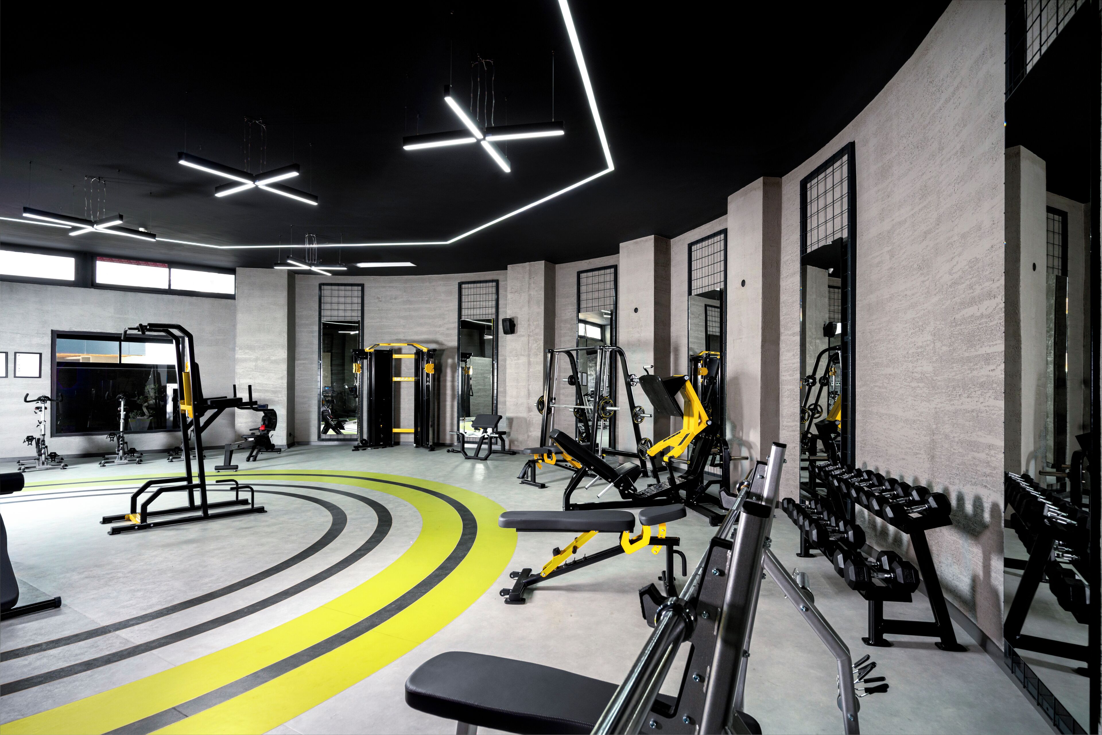 Un gimnasio moderno con diverso equipo de ejercicio, un banco central y una pista de atletismo amarilla.