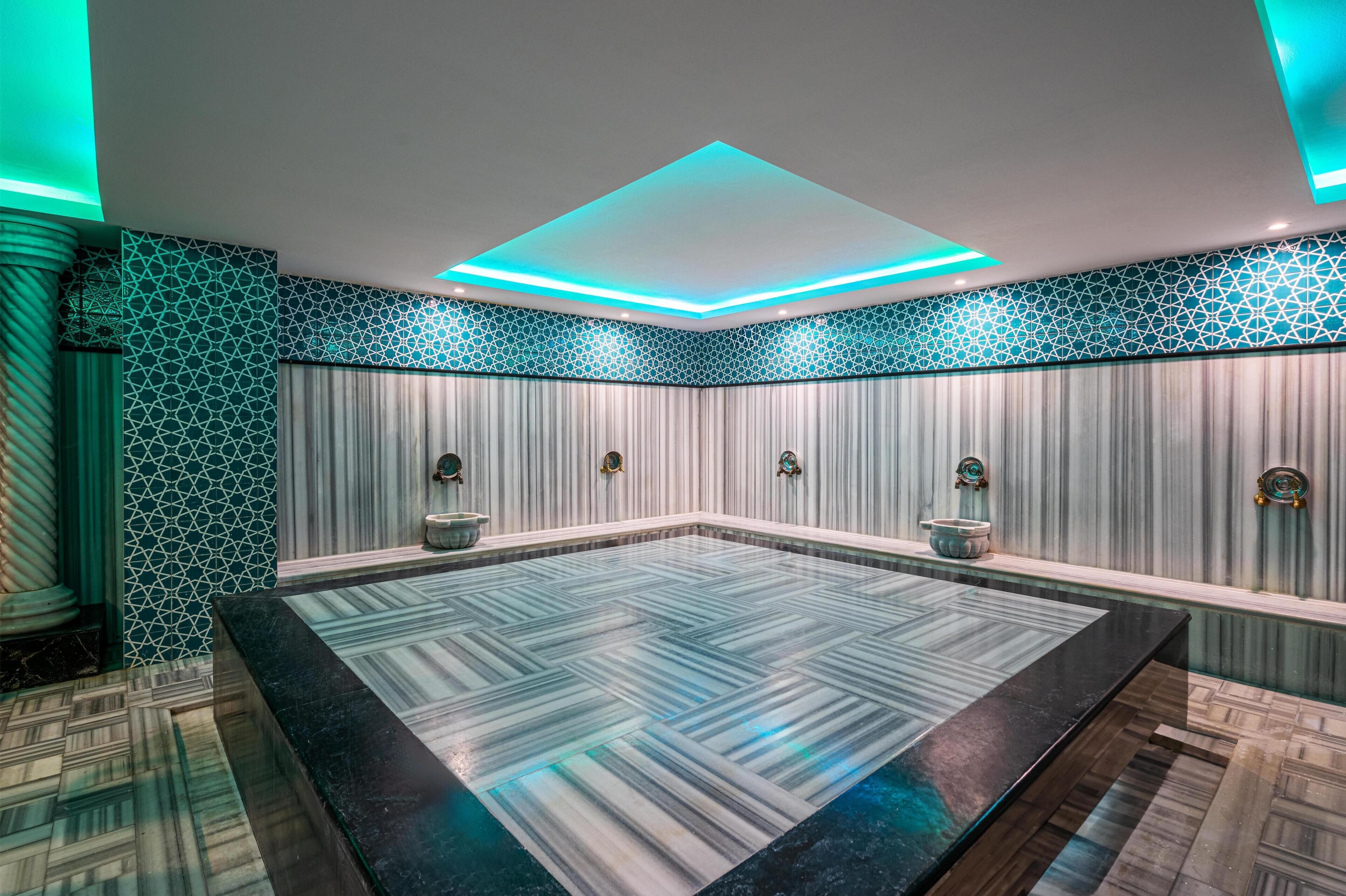 A modern spa room with a large rectangular hot tub, geometric patterned walls, and a ceiling with recessed lighting.