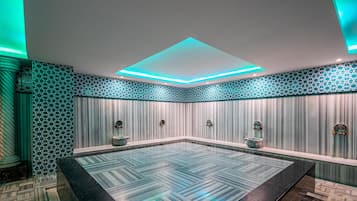 A modern spa room with a large rectangular hot tub, geometric patterned walls, and a ceiling with recessed lighting.