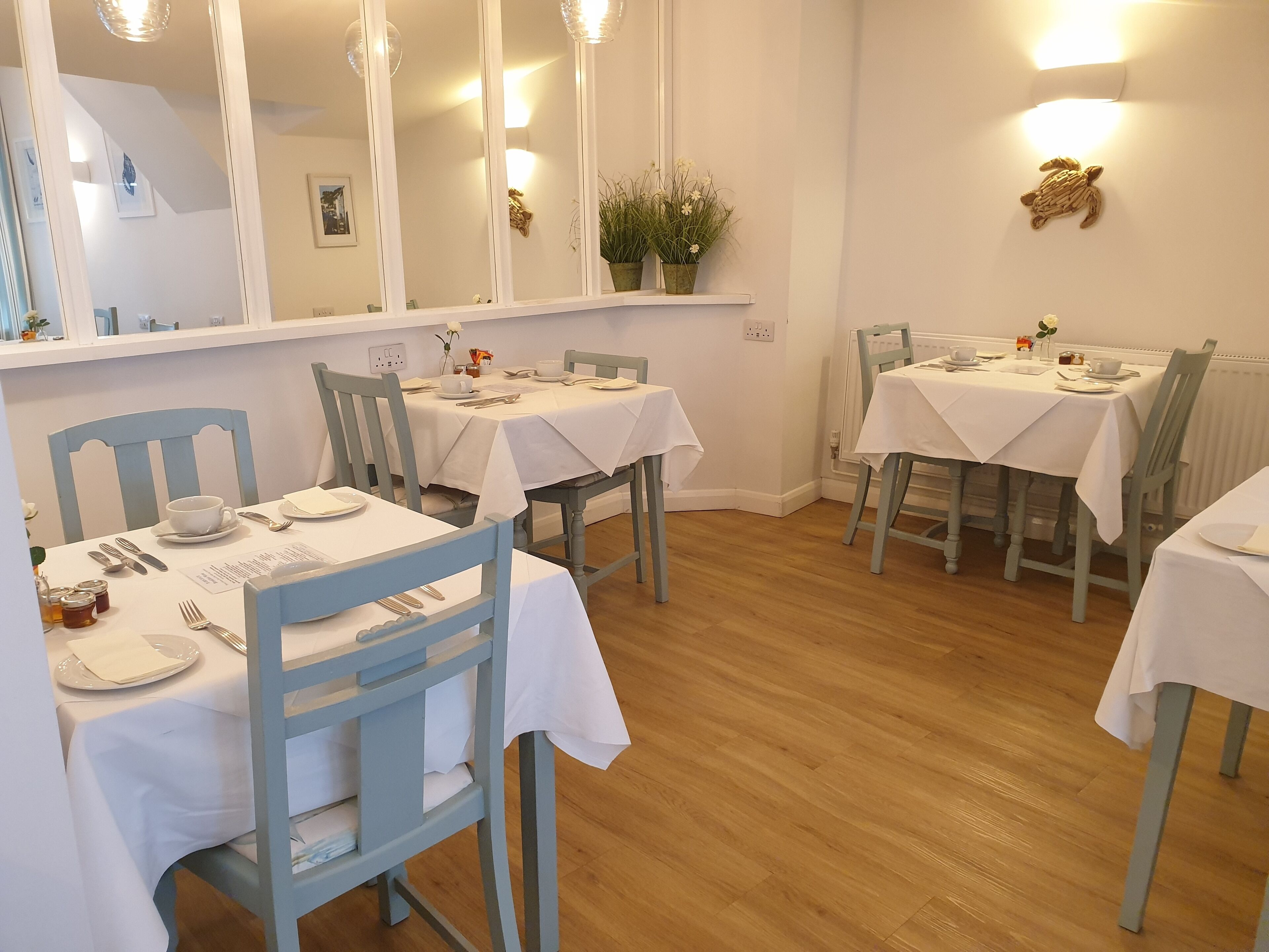 A dining area with white tablecloths, wooden chairs, and a mirrored wall.