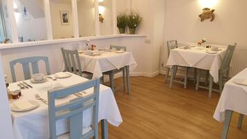 A dining area with white tablecloths, wooden chairs, and a mirrored wall.