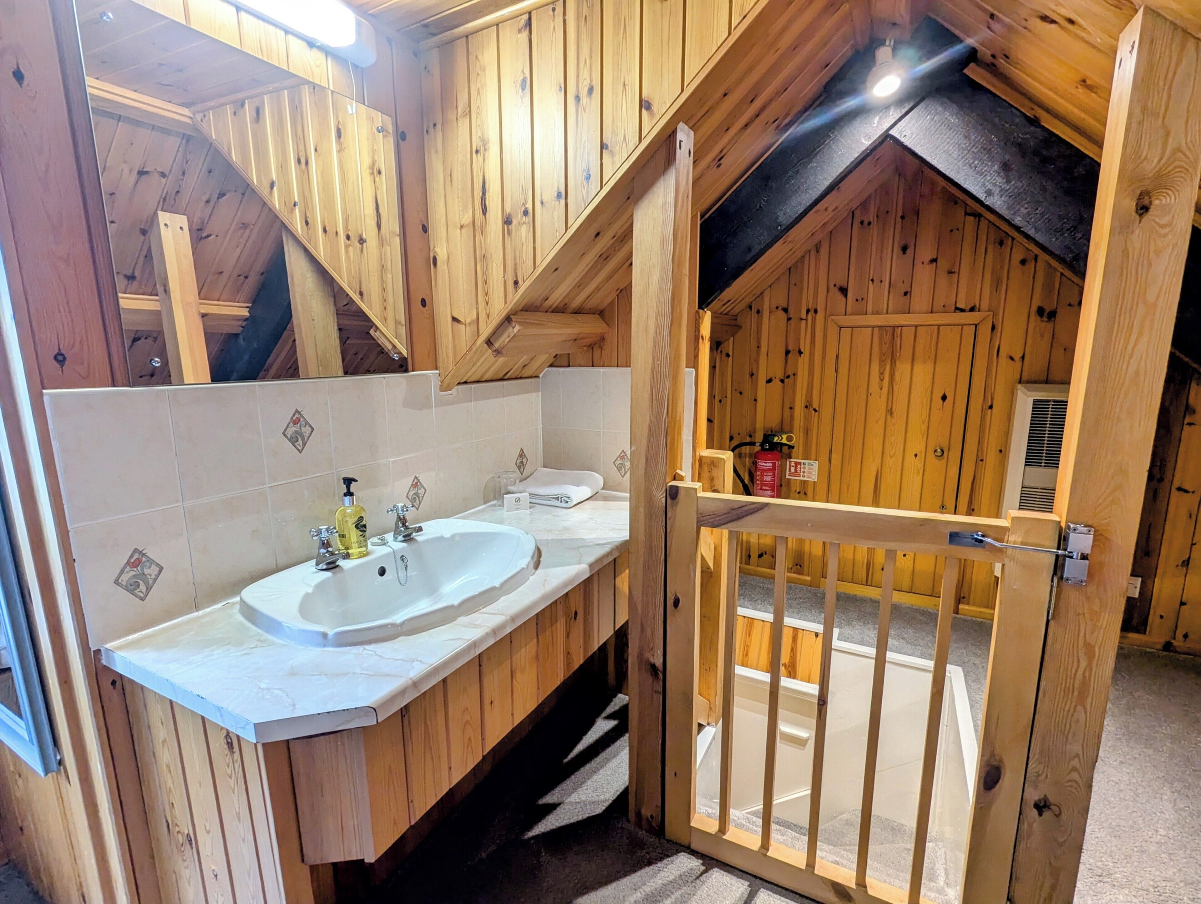 Een houten badkamer met een wastafel, spiegel en een houten deur die naar een andere kamer leidt.