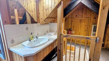 Un baño de madera con lavamanos, espejo y puerta de madera que da a otra habitación.