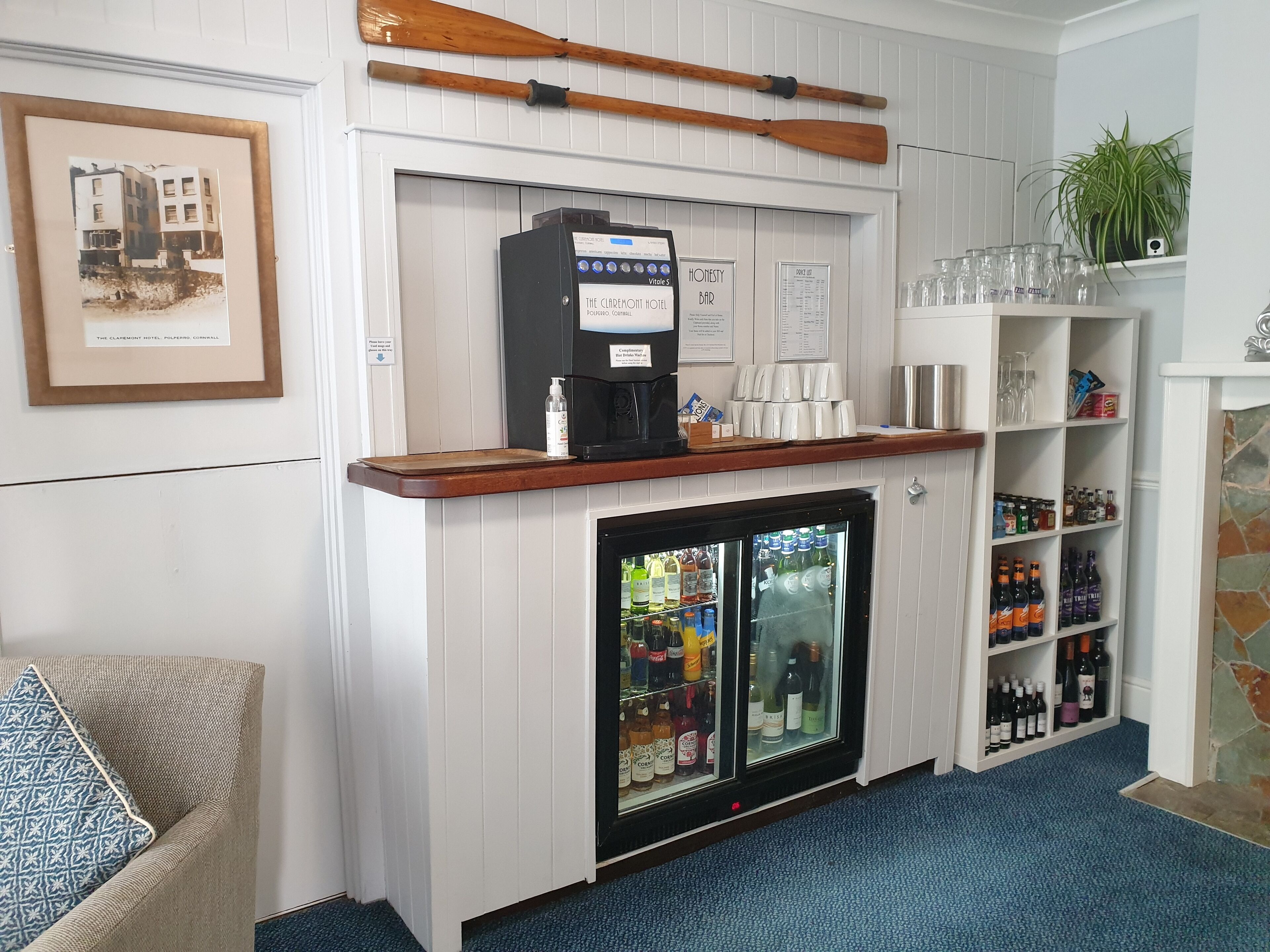 A bar area with a coffee machine, a mini-fridge stocked with beverages, and shelves with glasses and bottles.