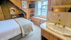 Un dormitorio de cabaña acogedor, con cama, baño con lavamanos y espejo, y ventana con cortinas.
