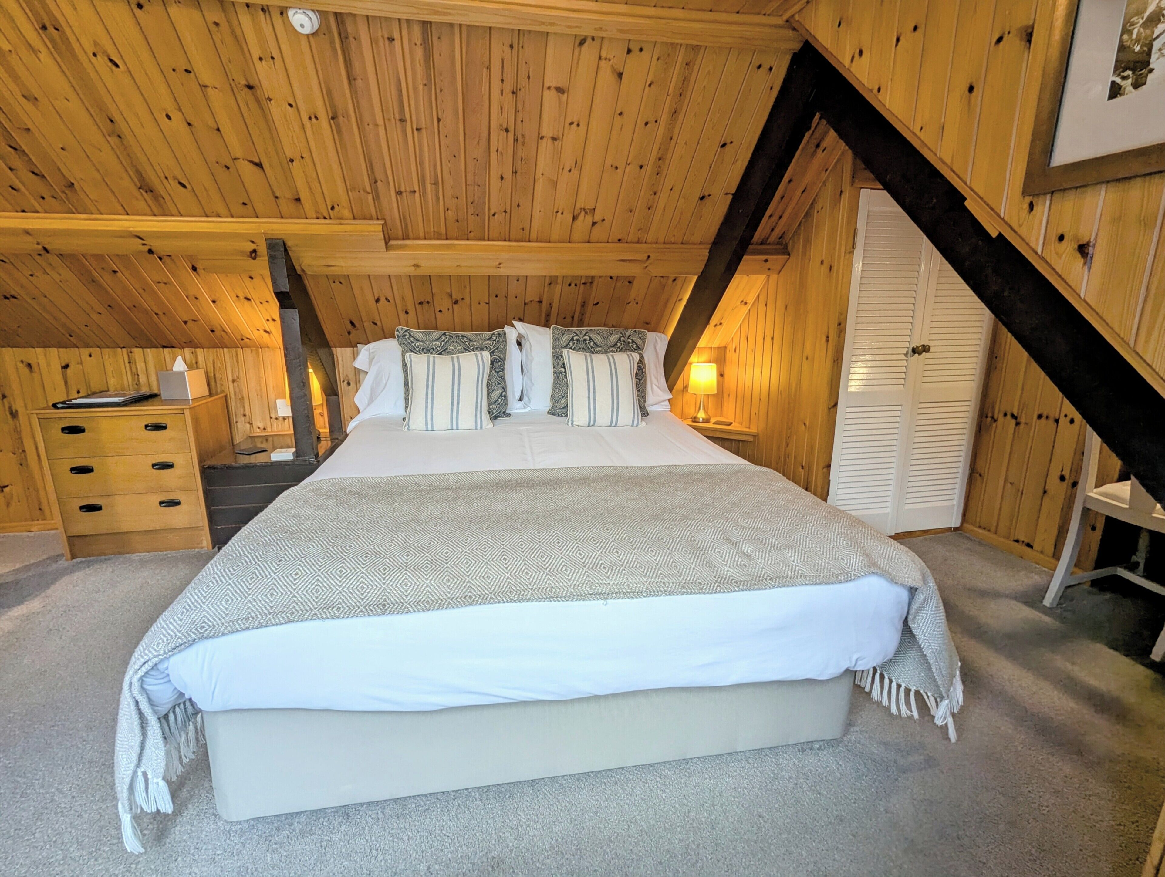A cozy attic bedroom with a large bed, wooden walls, and a sloped ceiling.