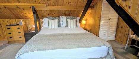A cozy attic bedroom with a large bed, wooden walls, and a sloped ceiling.