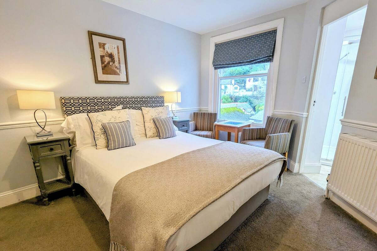 Ein ordentlich eingerichtetes Schlafzimmer mit einem großen Bett, Nachttischen, einem Sessel und einem Fenster mit Blick.