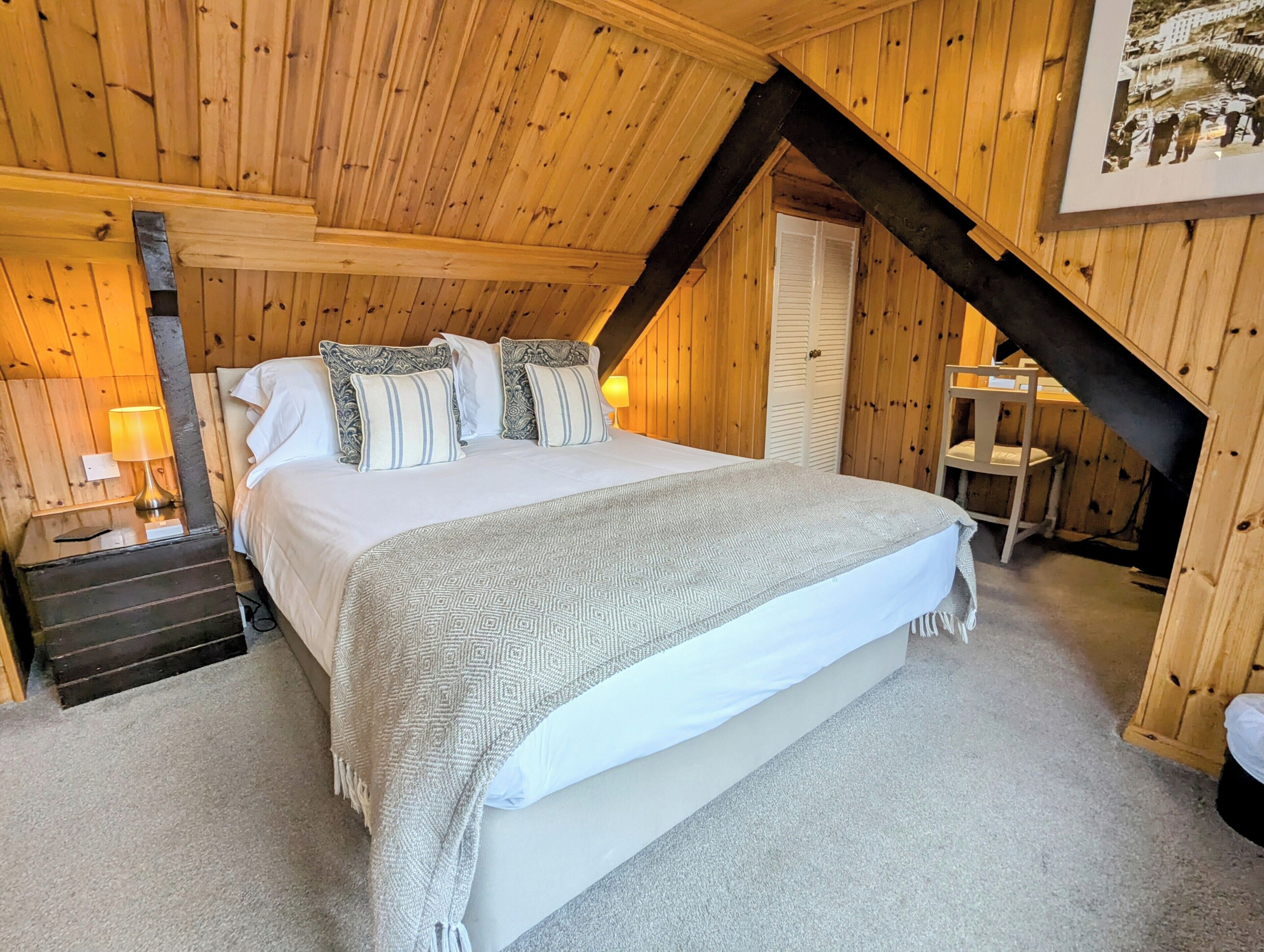 A cozy bedroom with a large bed, wooden walls, and a sloped ceiling.