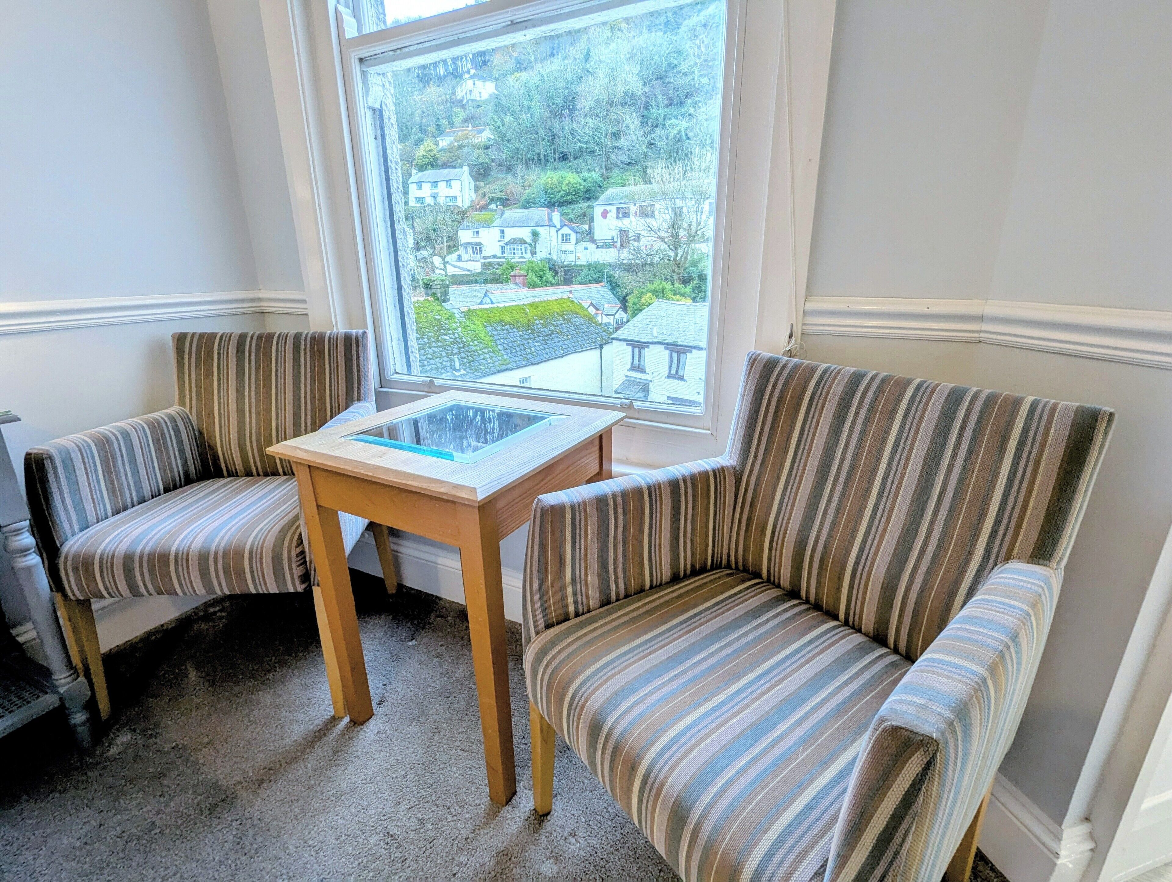 A corner seating area with two striped armchairs and a small wooden table with a glass top.