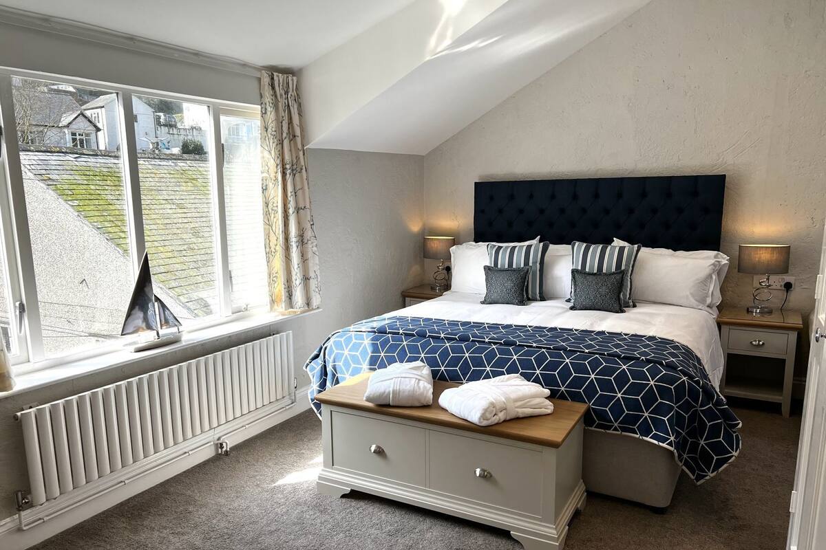 Ein Schlafzimmer mit Bett, Nachttischen, Heizkörper, Fenster und Blick ins Freie.