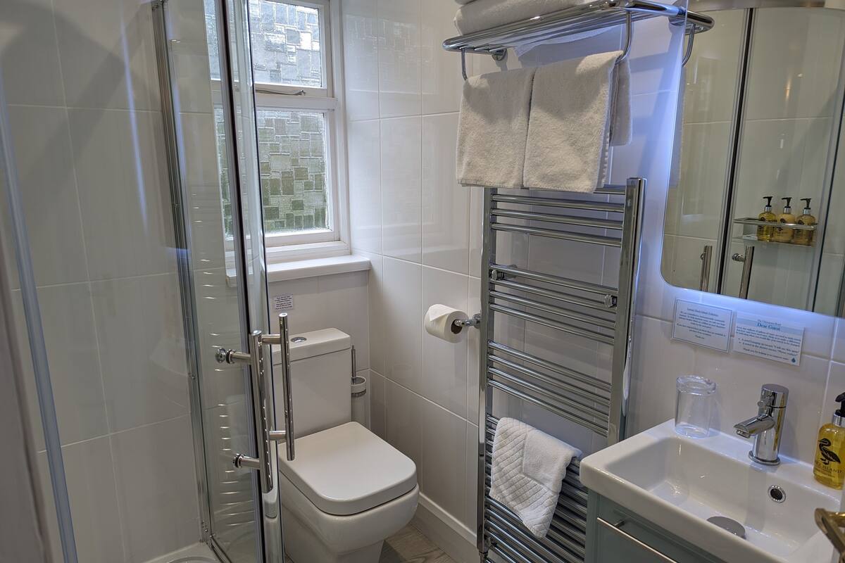 Ein Badezimmer mit Duschkabine, Toilette, Handtuchhalter, Waschbecken und einem Fenster.