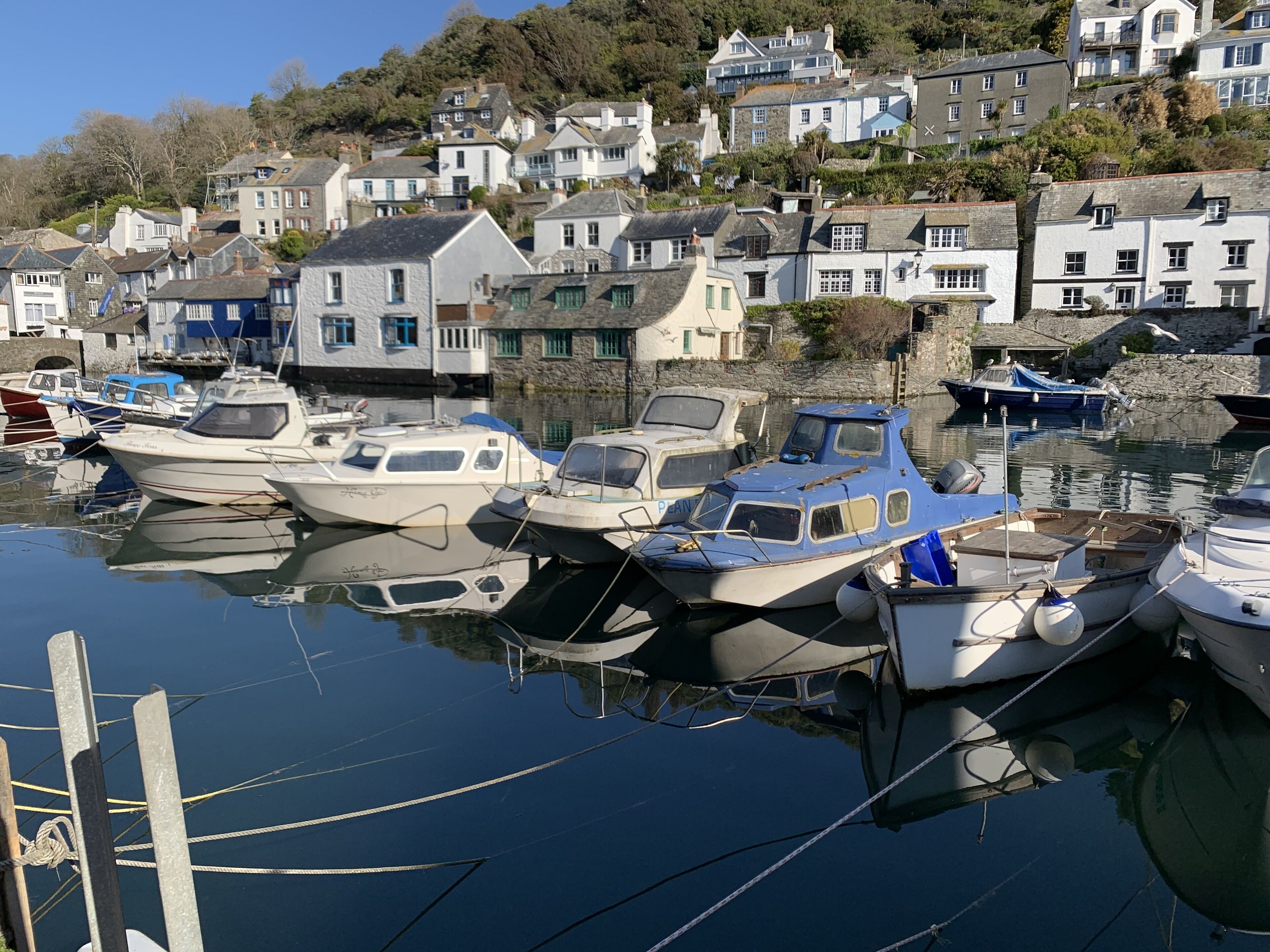 A marina with several boats docked, surrounded by houses with stone walls and pitched roofs.