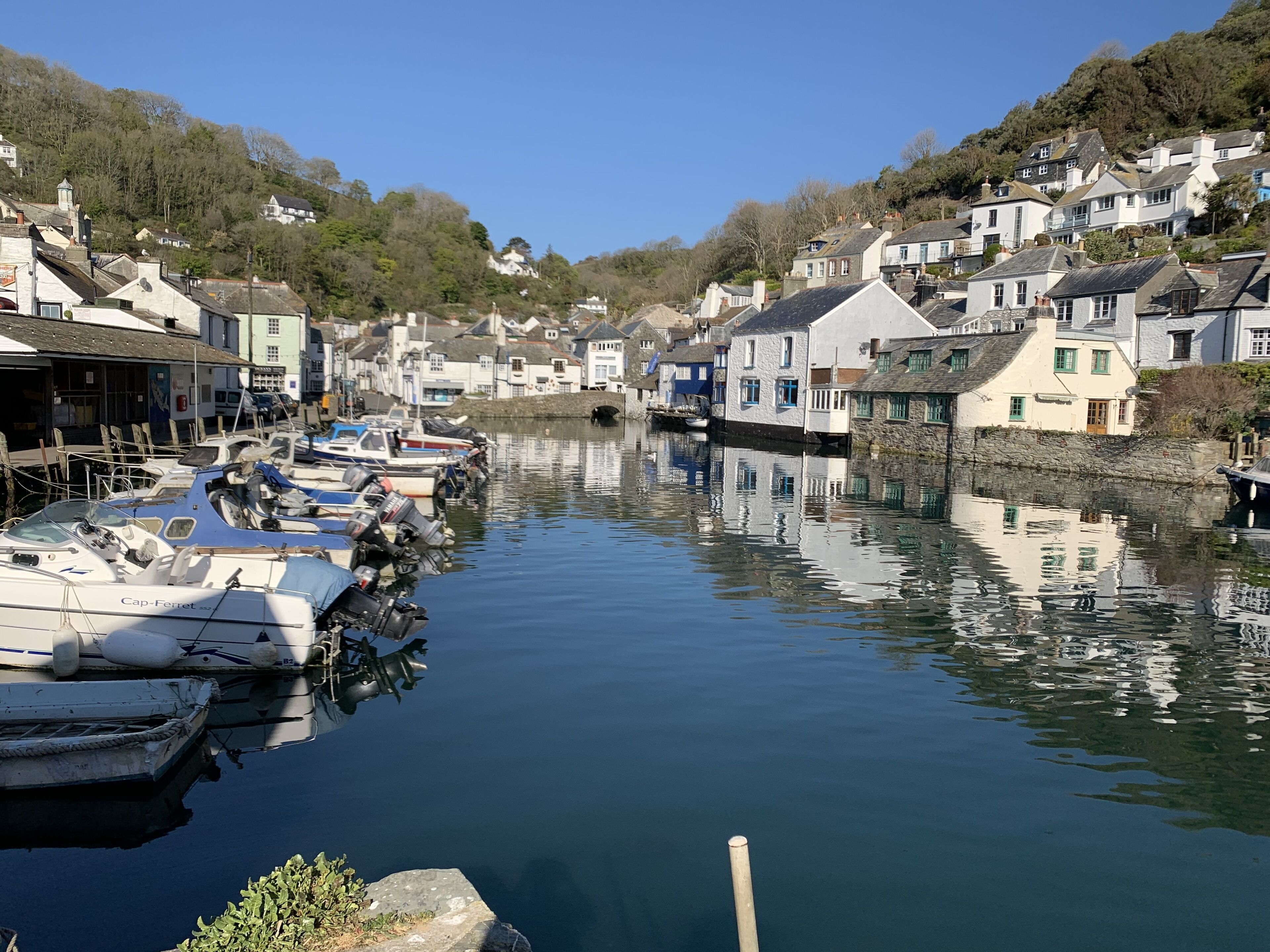 A calm harbor with boats docked along the sides, surrounded by houses with stone walls and pitched roofs.
