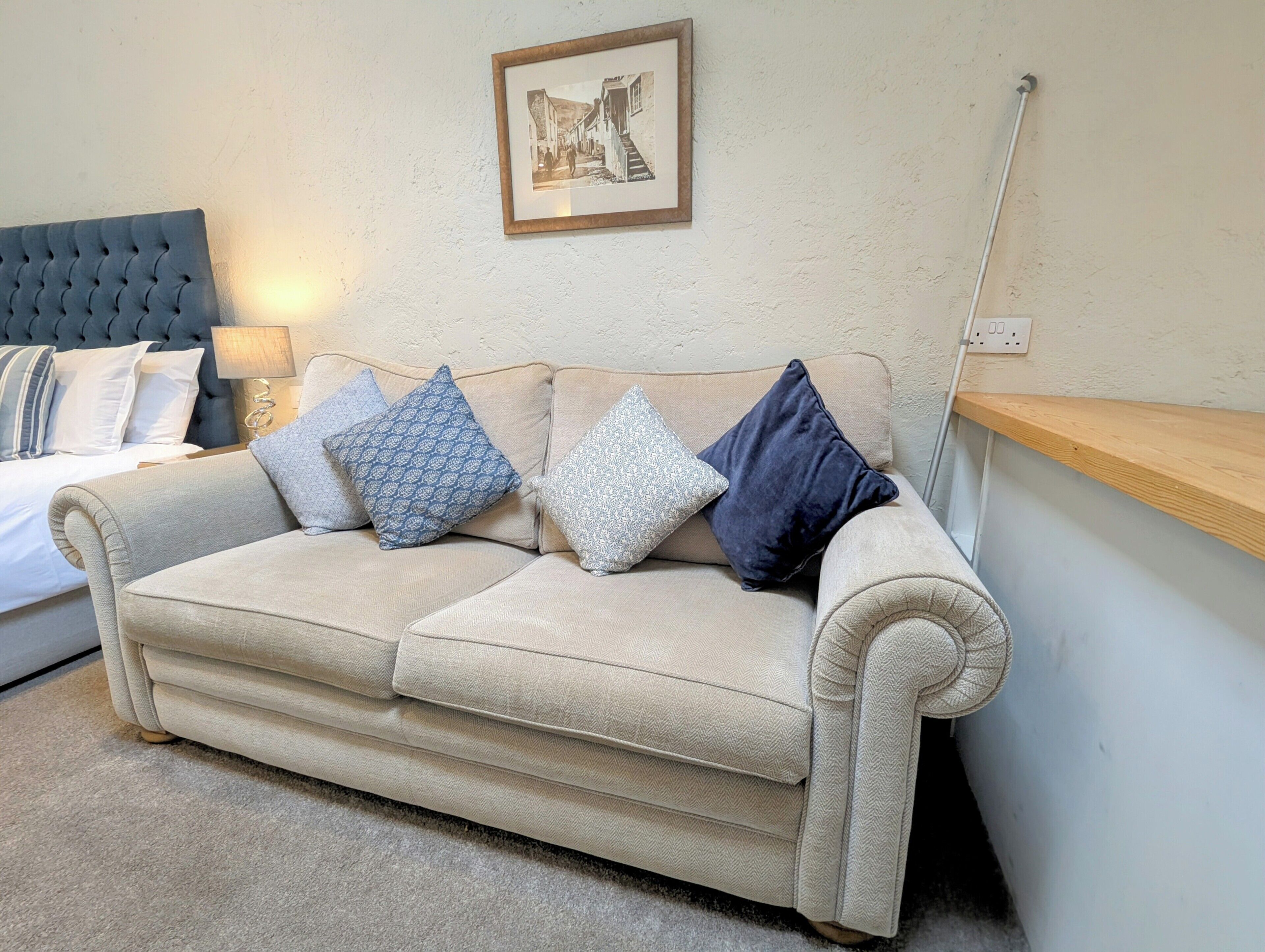 A beige sofa with patterned cushions, a framed picture on the wall, and a wooden shelf.