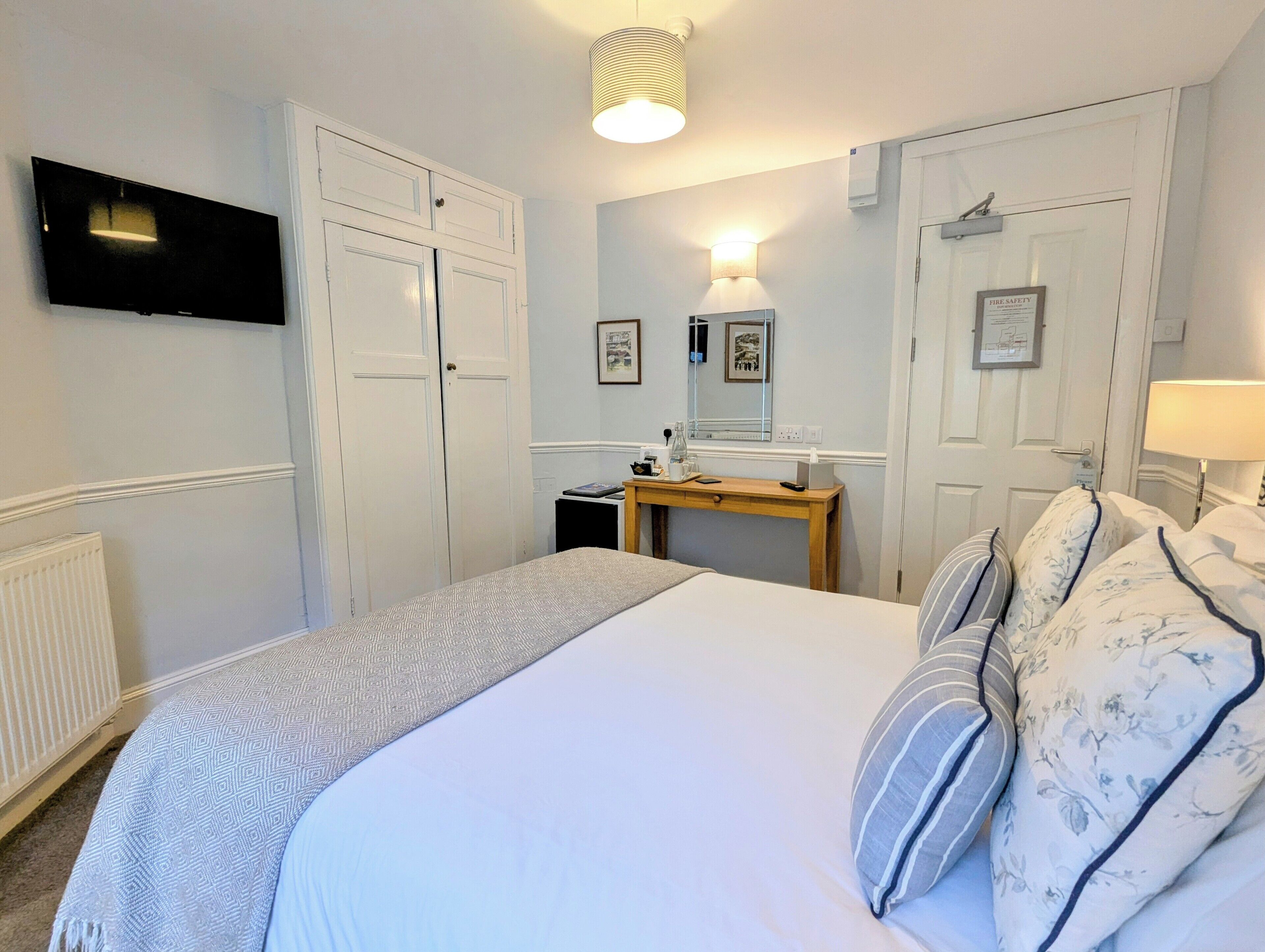 A bedroom with a bed, bedside tables, a desk, a television, and a mirror.