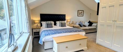 A bedroom with a large bed, a sofa, a chest of drawers, and a wardrobe.