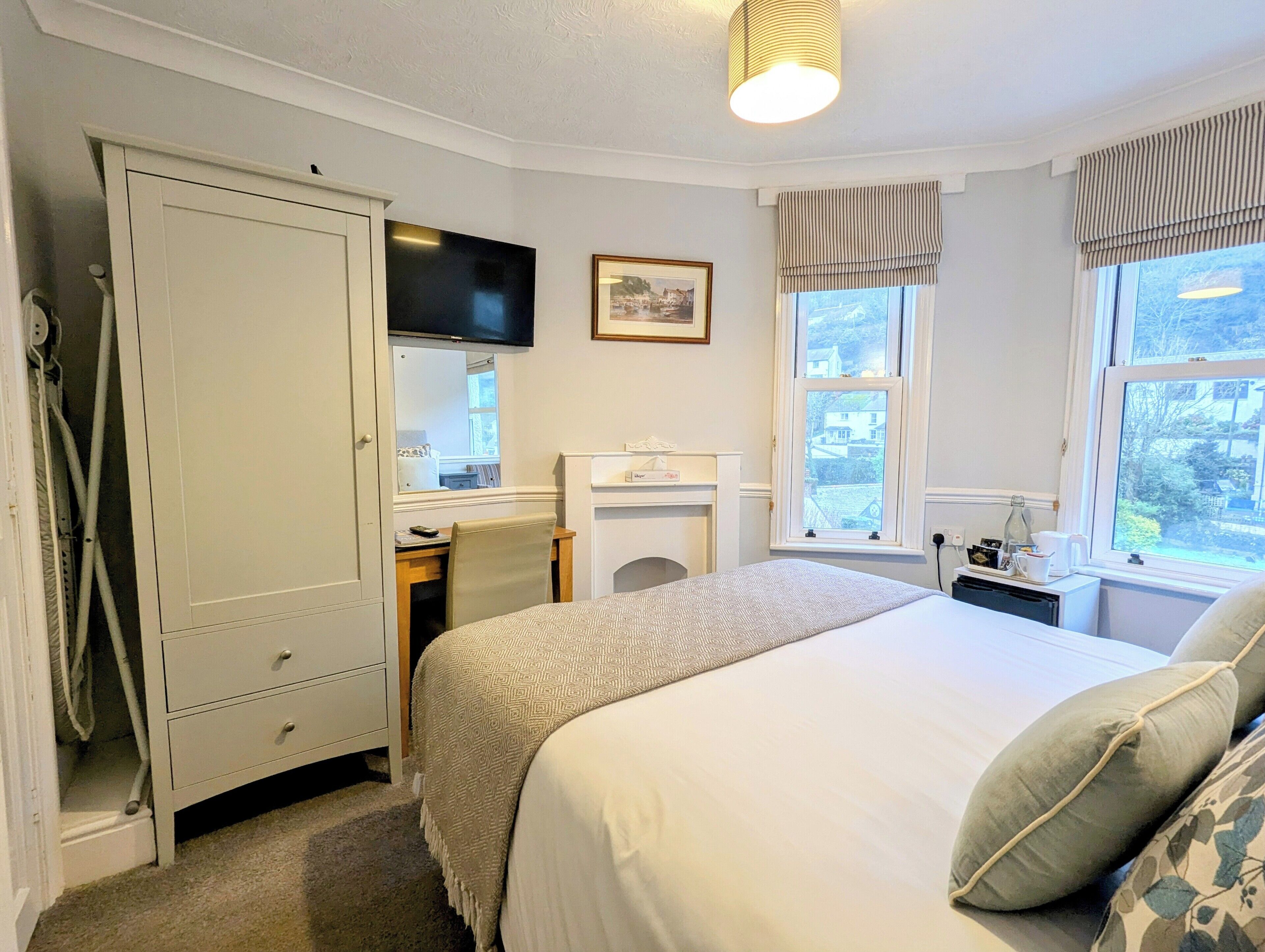 Een slaapkamer met een bed, een bureau, een kledingkast, een televisie en een raam met uitzicht op huizen.