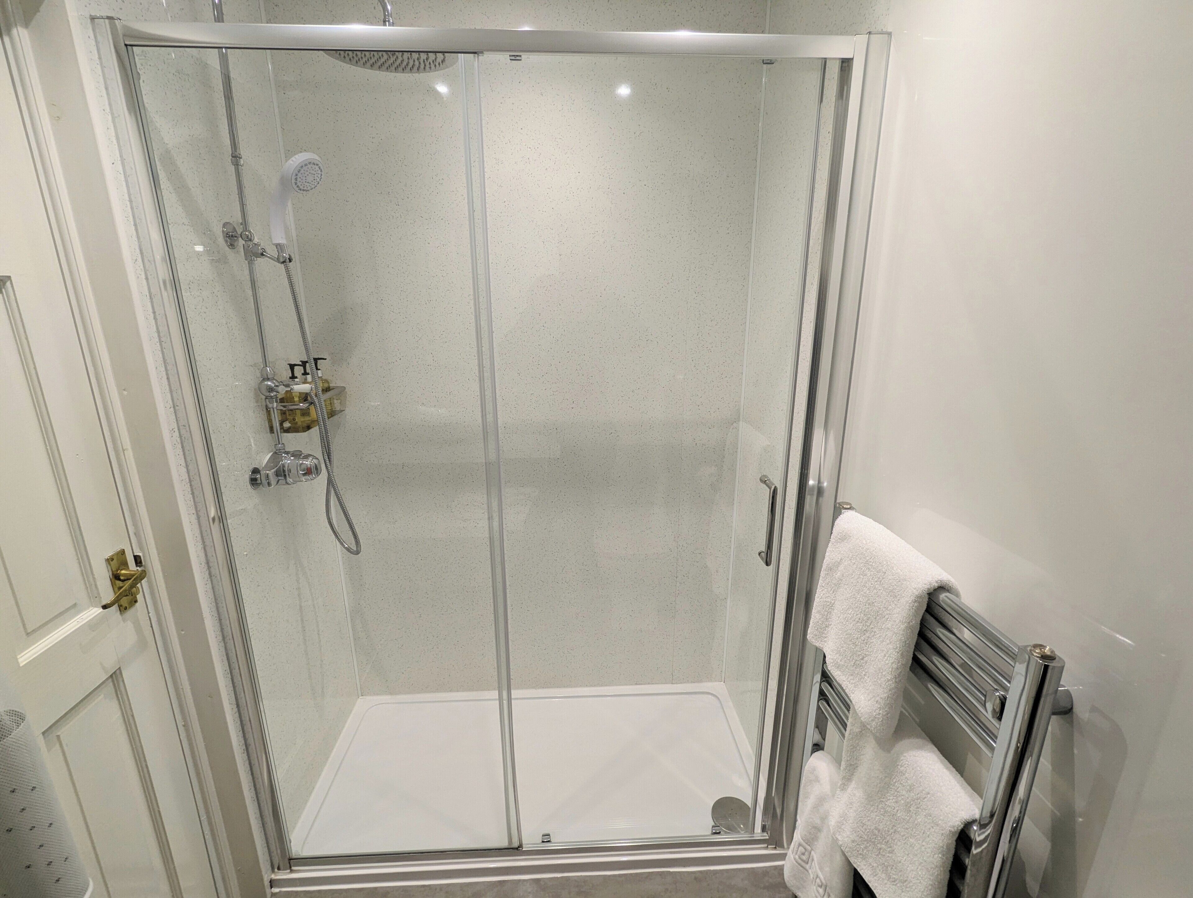 A glass-enclosed shower with a white tiled wall, a towel rack, and a door with a brass handle.
