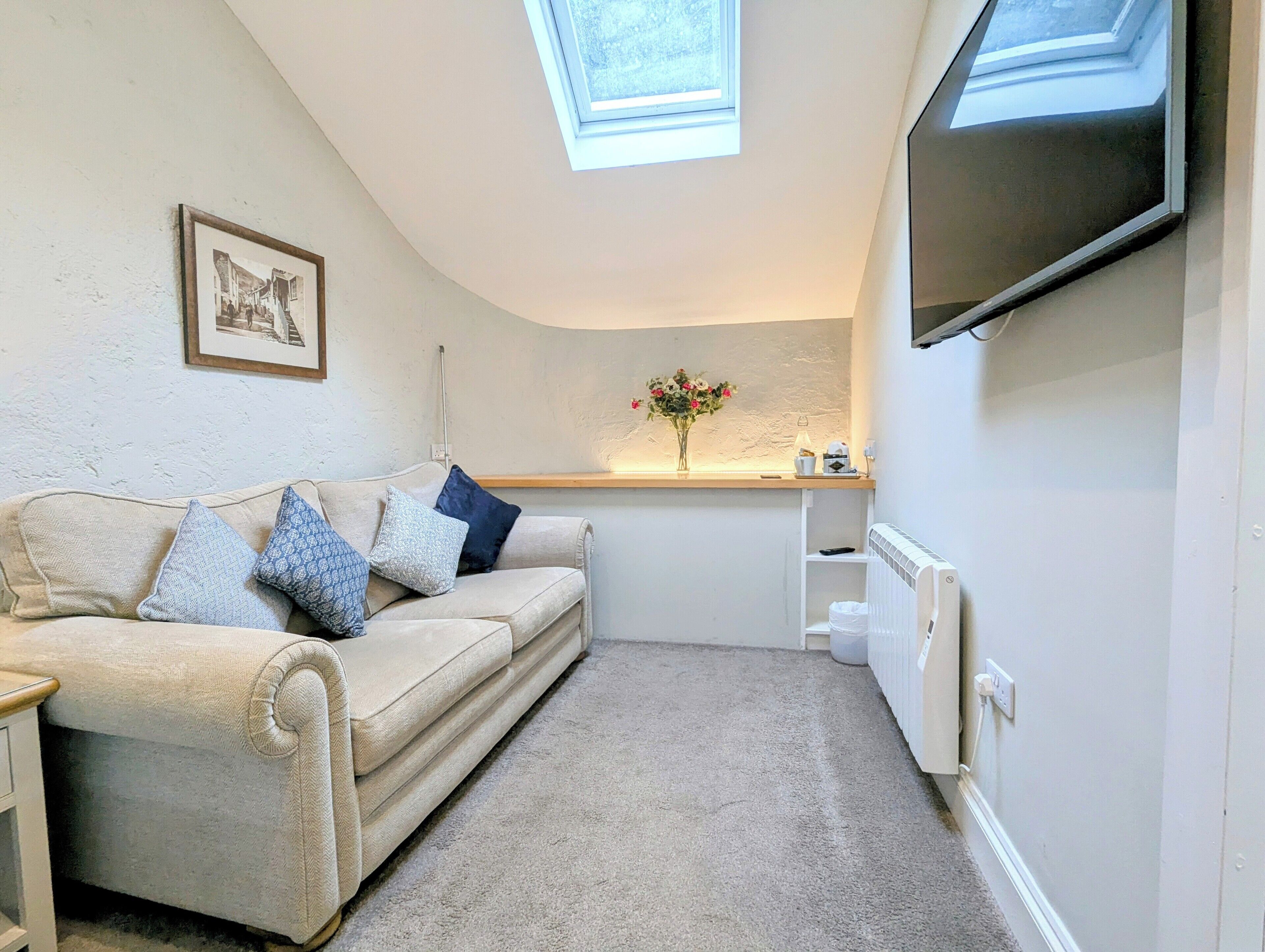 A cozy room with a sofa, a flat-screen TV, a framed picture, and a small table with a vase of flowers.