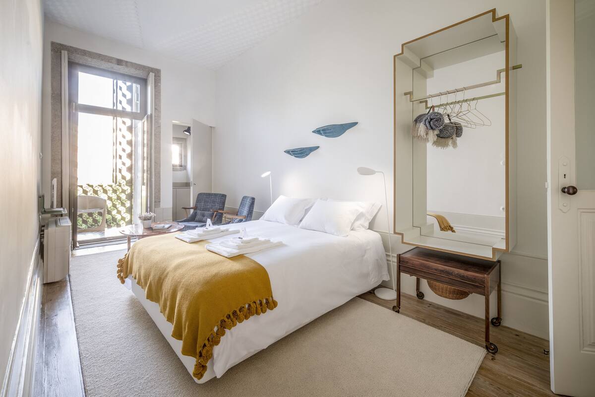 A hotel room with a bed, a desk, a chair, a large mirror, and a view of the outside.