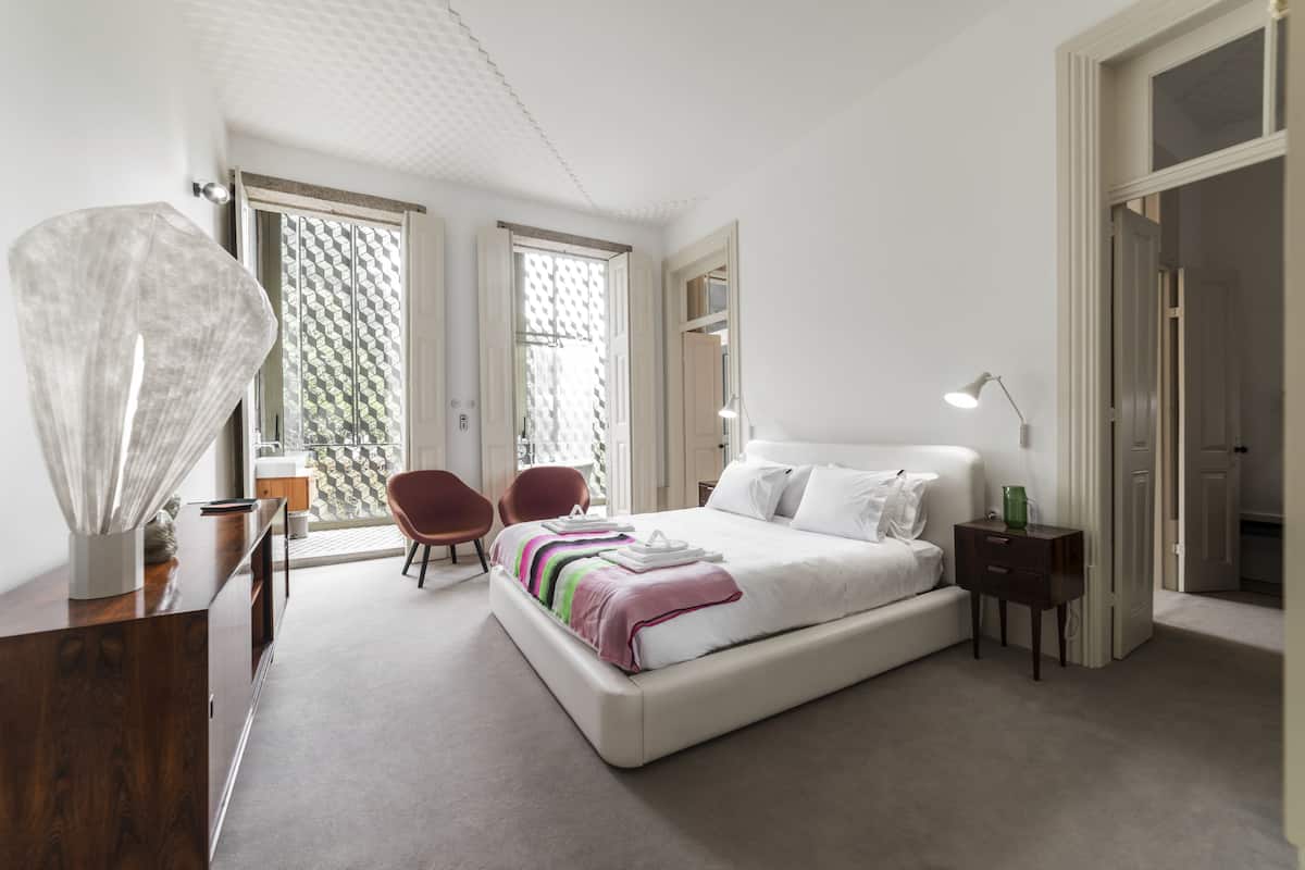 A modern bedroom with a large bed, two chairs, a bedside table, and a desk.