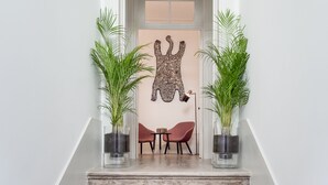 Uma escadaria com design moderno que leva a um quarto com decoração minimalista, incluindo uma obra de arte com padrão e duas plantas em vasos.