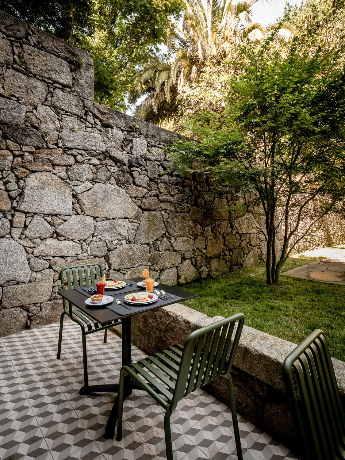 An outdoor dining area with a stone wall, a tiled floor, and green chairs.