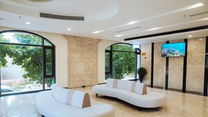 Un lobby moderno con dos sofás blancos, ventanas amplias, un televisor de pantalla plana y suelo de mármol.