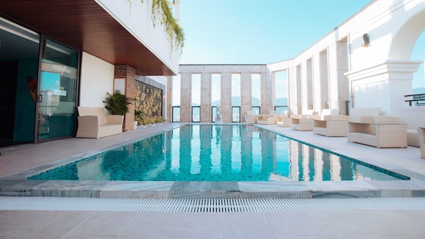 A modern indoor pool area with a clear view of the sky, surrounded by lounge seating and a glass wall. - Danaciti Hotel (Da Nang)