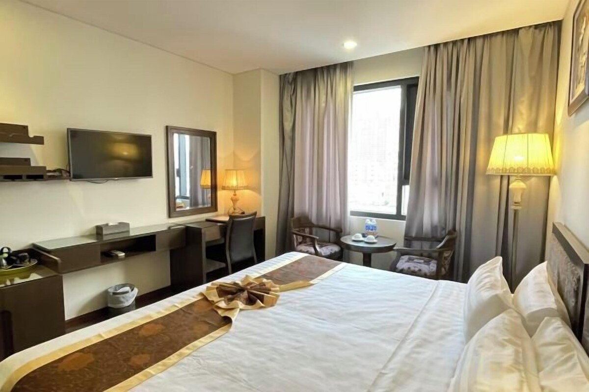 A hotel room with a bed, a desk, a chair, a television, and a window with curtains.