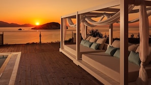 A wooden deck with a white outdoor seating area, overlooking a sunset over water.