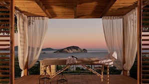 A wooden deck with a bench and two lanterns, overlooking a body of water and a distant island.