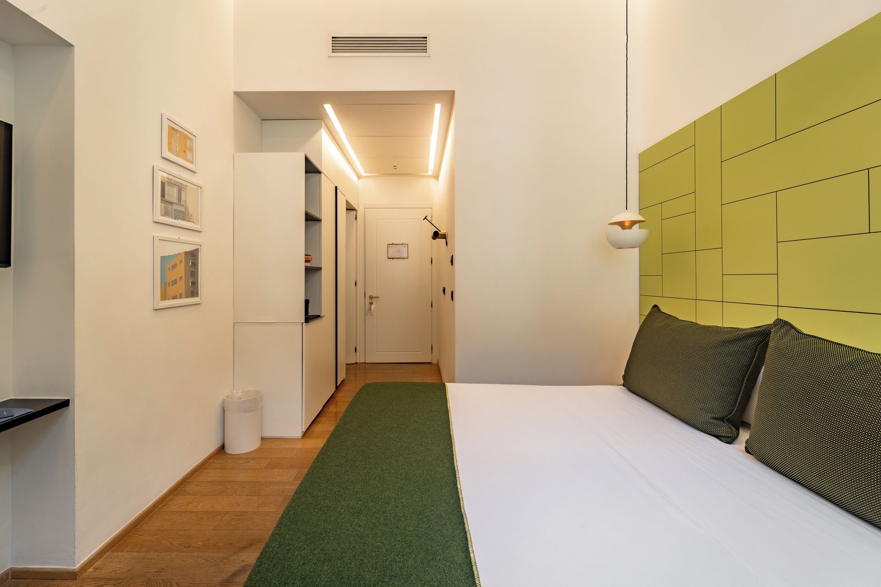 A bedroom with a green accent wall, a white bed, and a hallway leading to a bathroom.