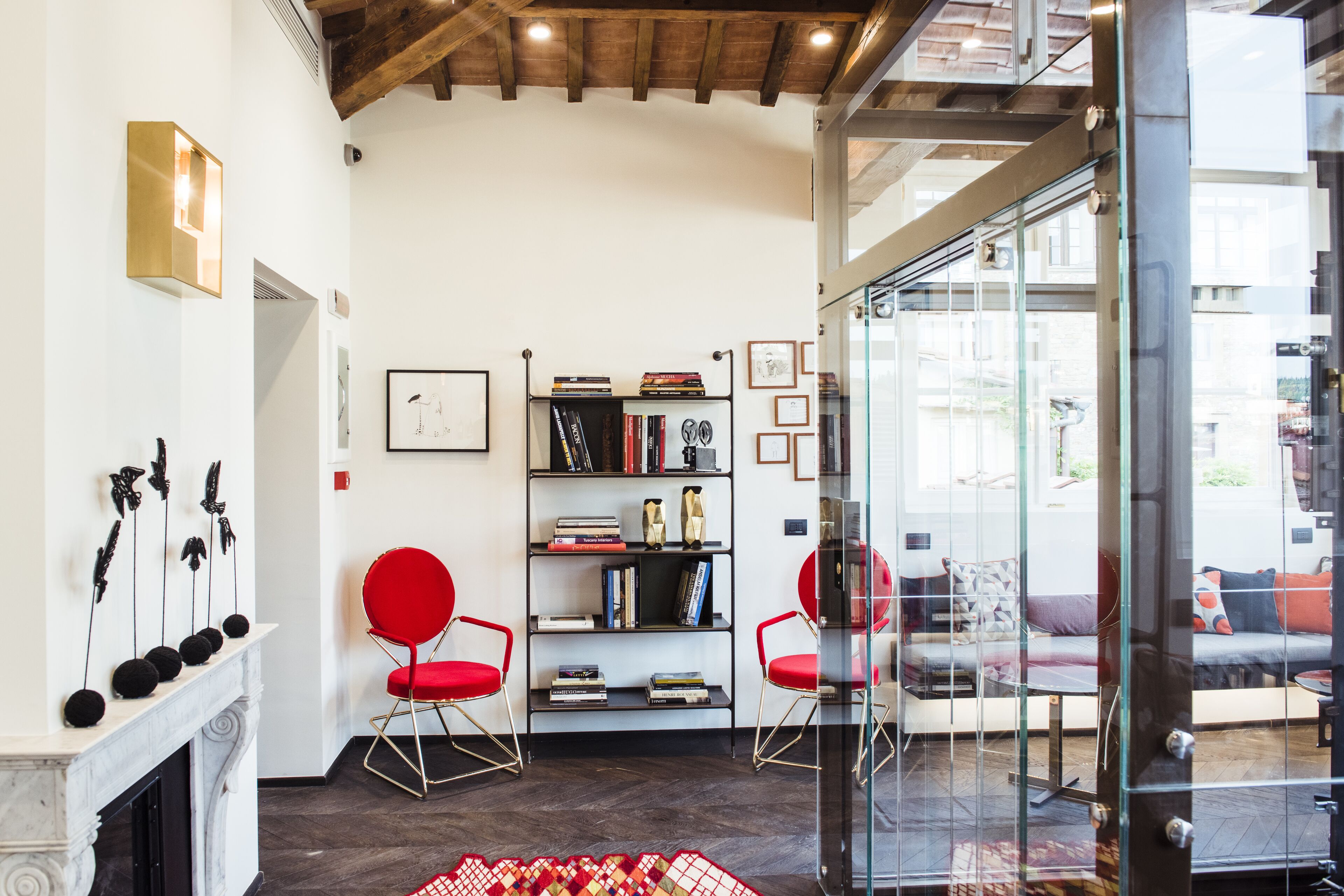 Una sala moderna con chimenea, sillas rojas, una estantería y un ventanal que da a un espacio exterior.