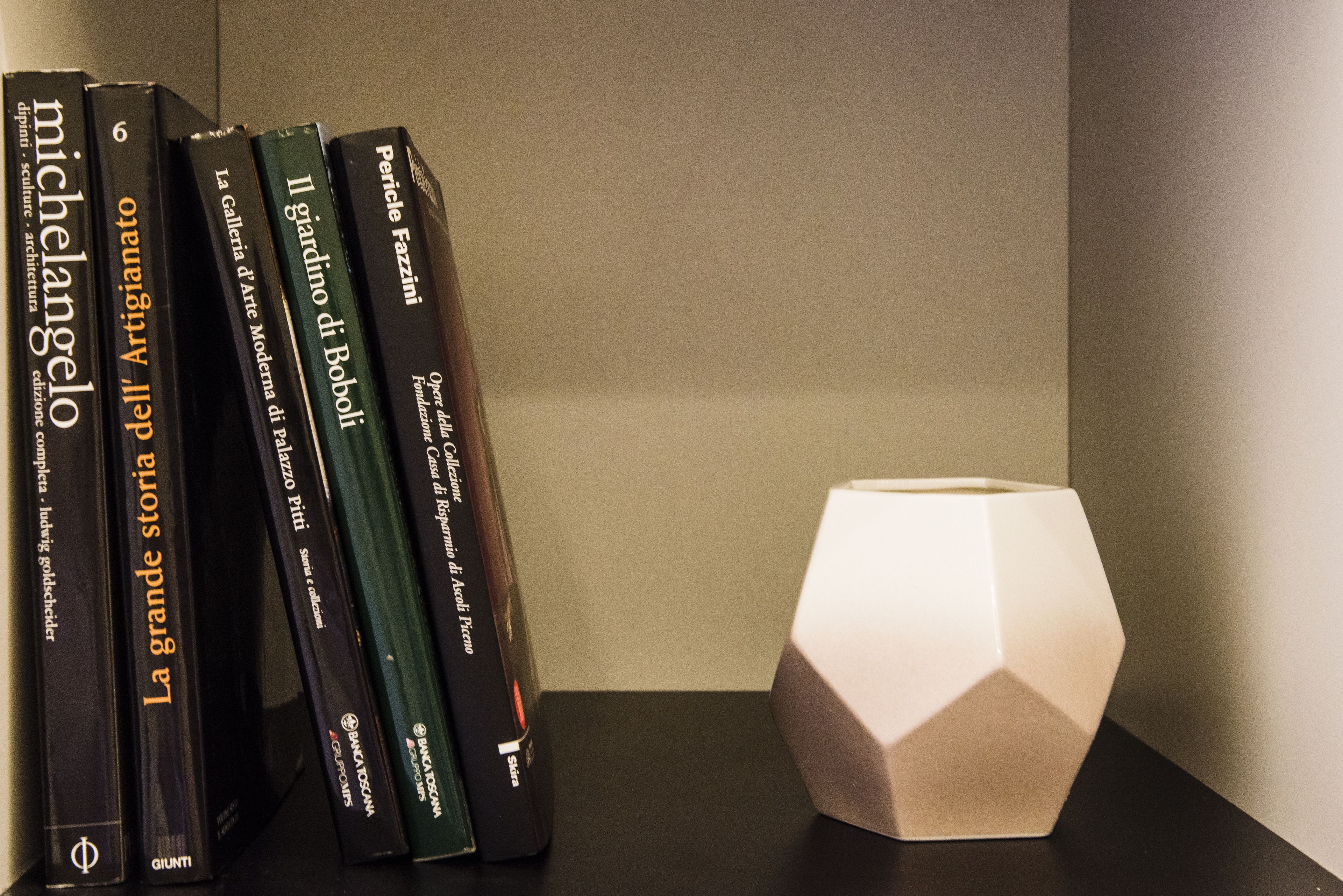 Una libreria con libri e un vaso bianco geometrico.