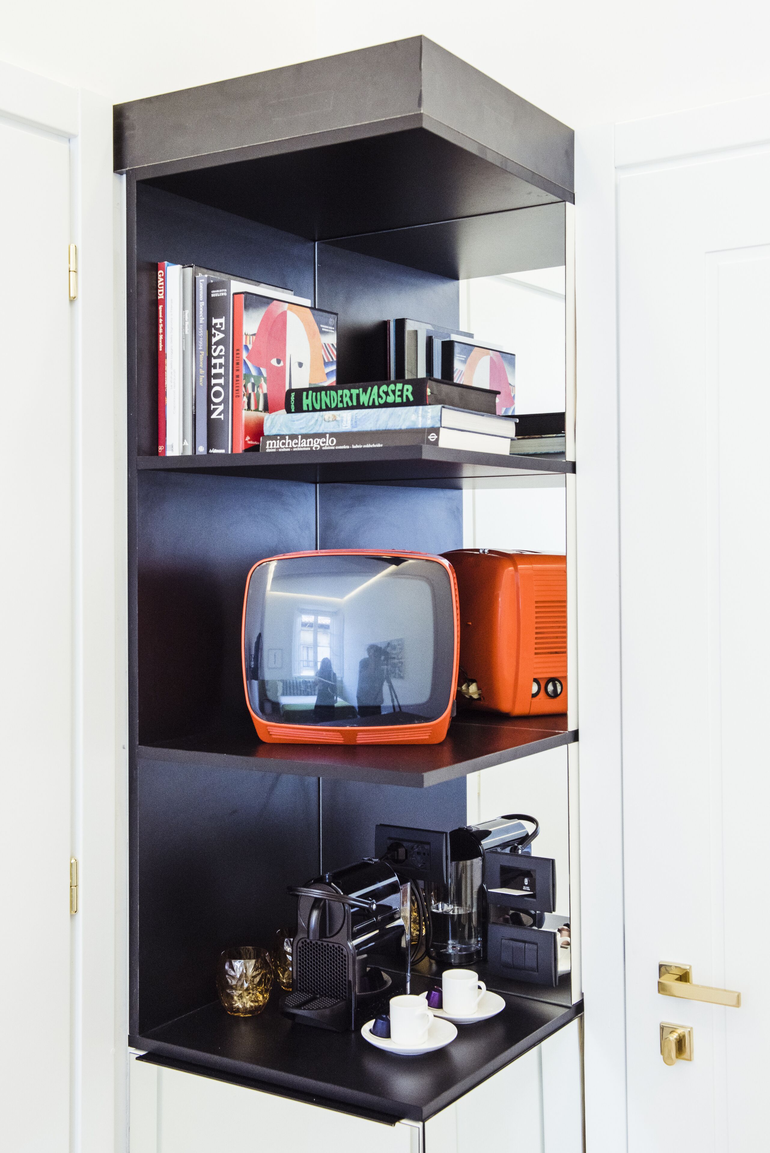Una estantería negra con libros, un televisor retro y una cafetera.
