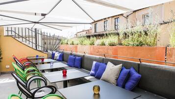 An outdoor seating area with tables and chairs, a covered section, and a staircase leading to an upper level.