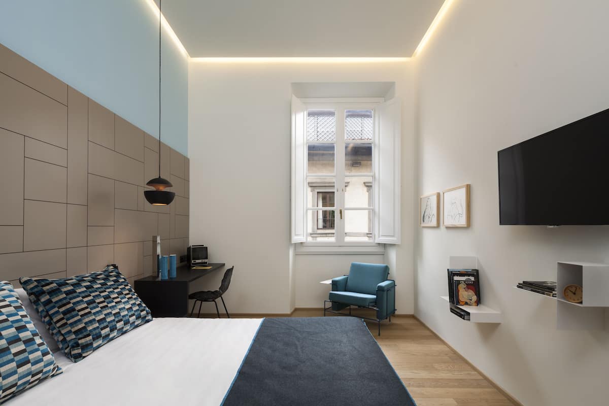 Un dormitorio moderno con cama, escritorio, silla, televisor y ventana.