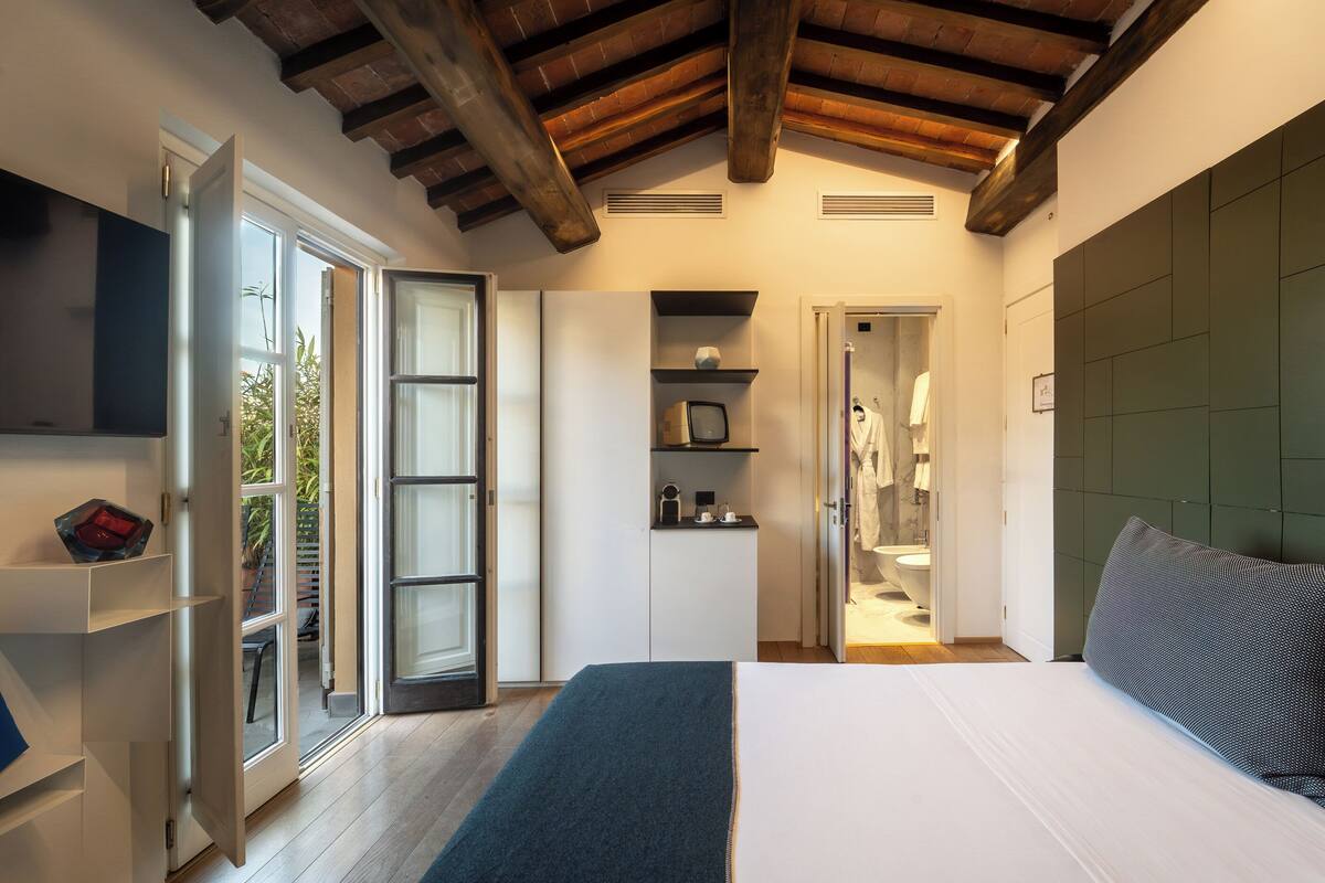 Un dormitorio con una cama grande, televisión, armario y baño visible a través de una puerta abierta.