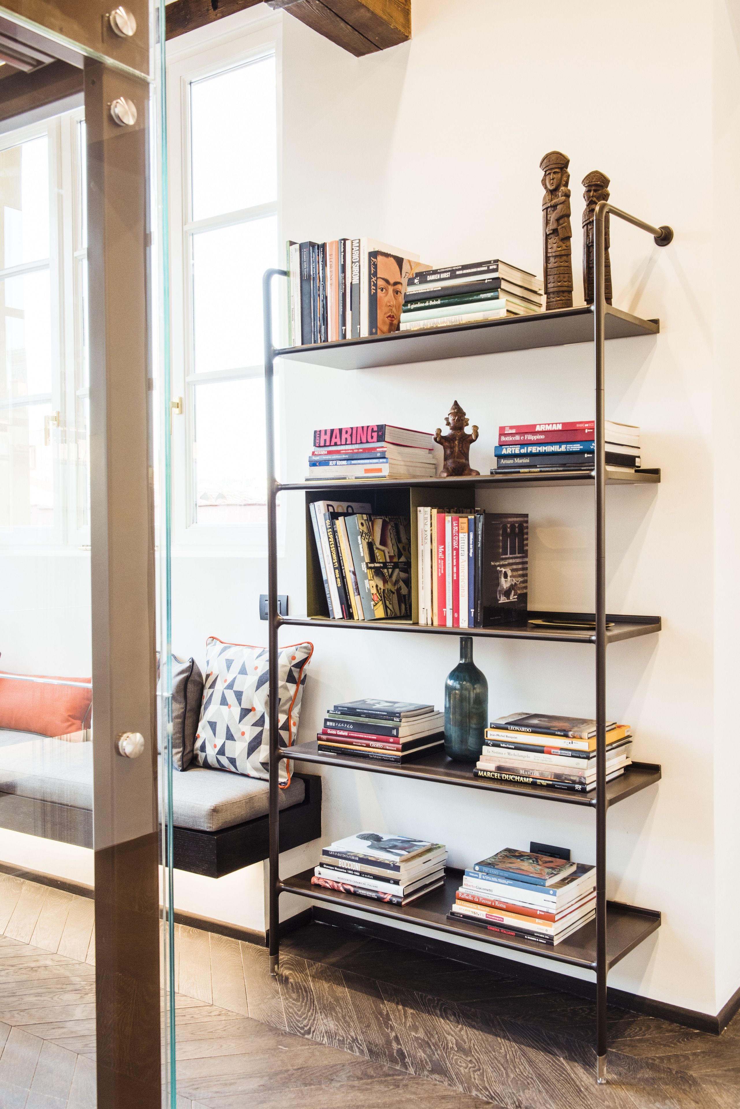 A bookshelf with books and decorative items, a patterned cushion, and a wooden floor.