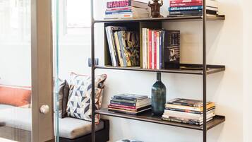 A bookshelf with books and decorative items, a patterned cushion, and a wooden floor.