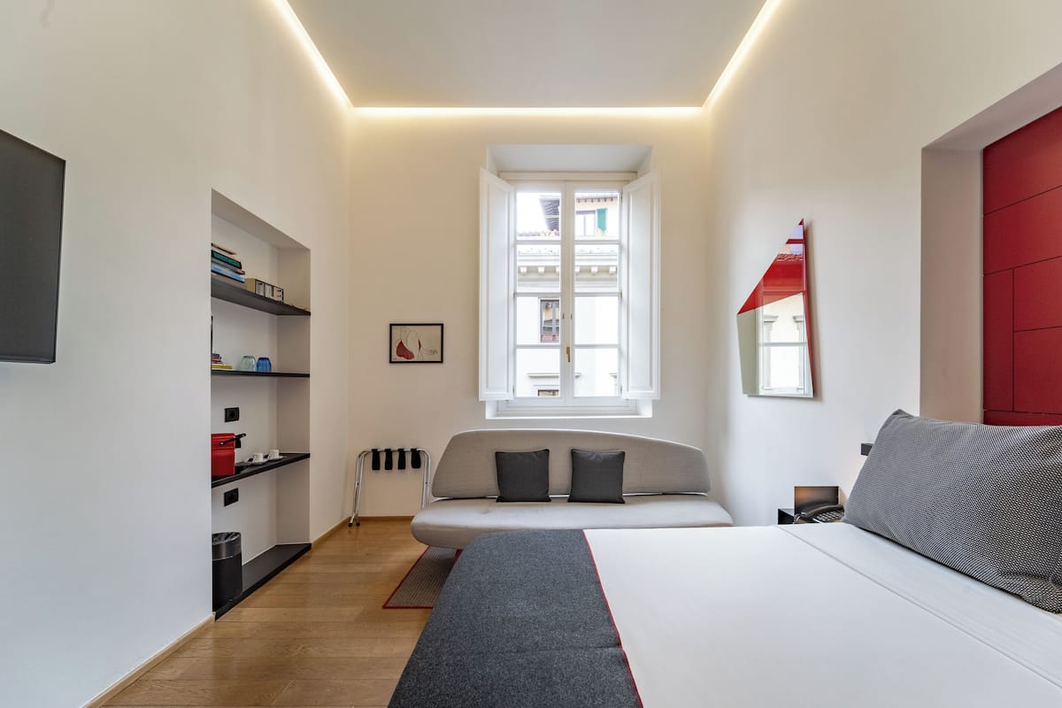 Un dormitorio moderno con cama, sofá, ventana y estantería.