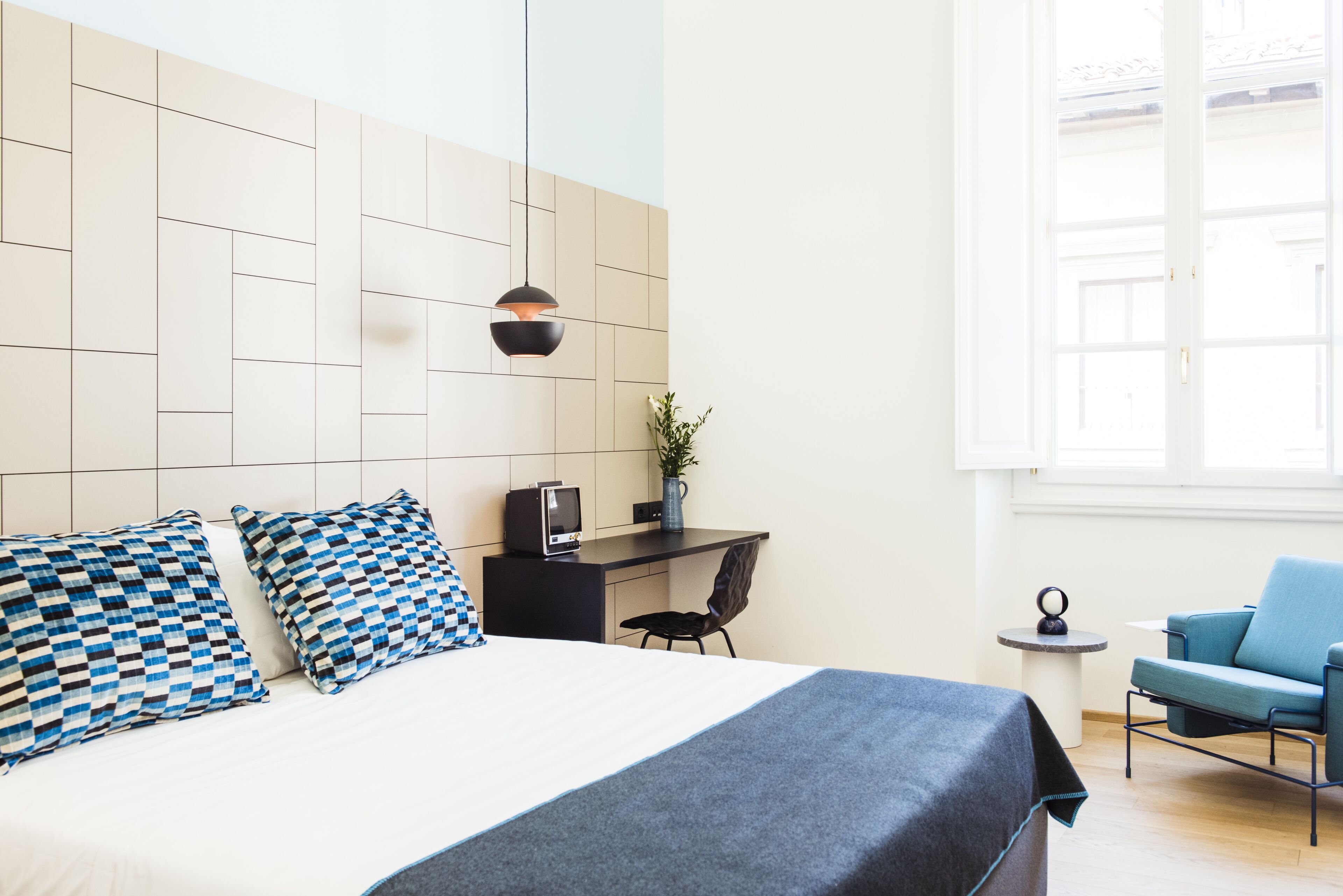 A modern hotel room with a large bed, a desk, a chair, and a window.